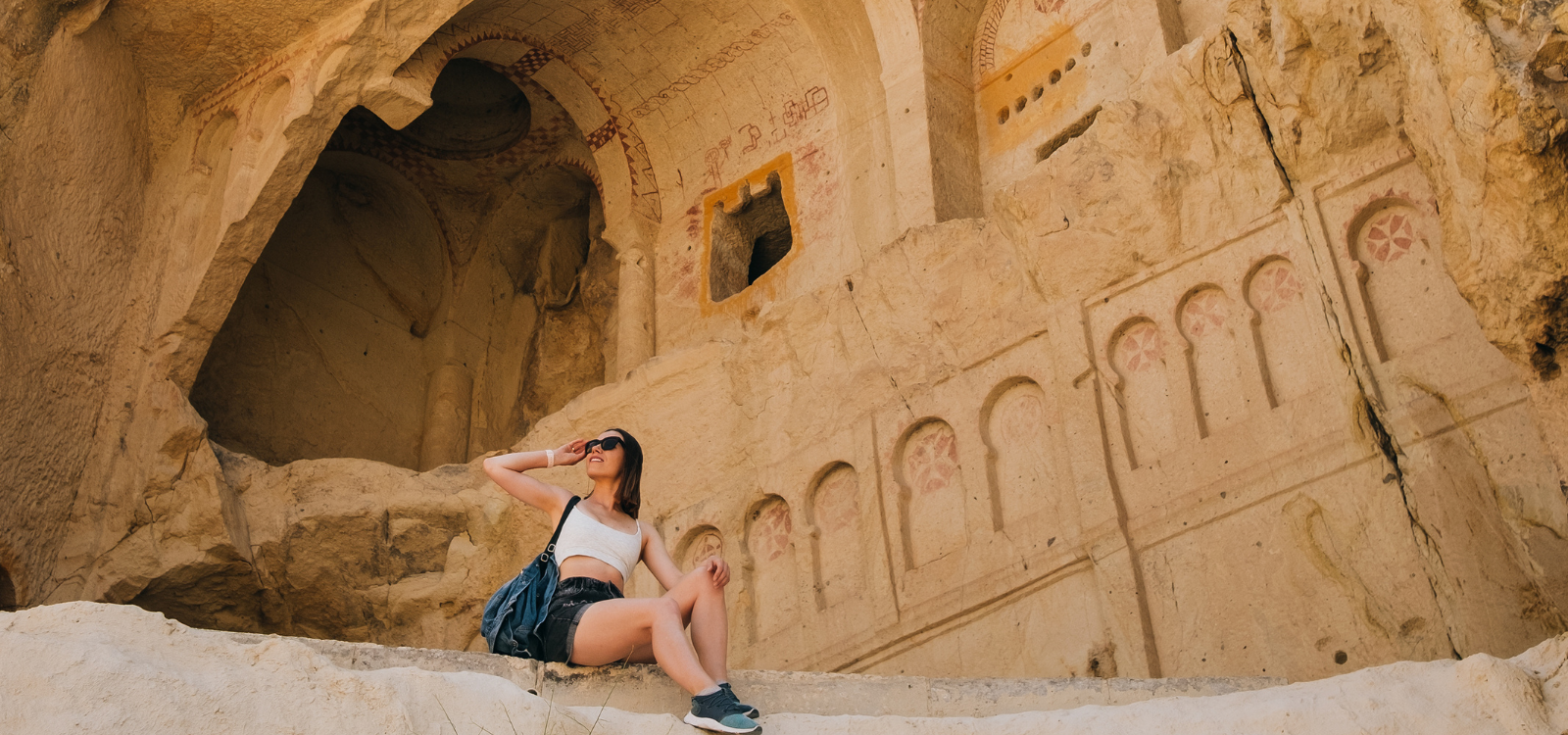 A tourist lady sits under some of the carved caves of Petra in Jordan