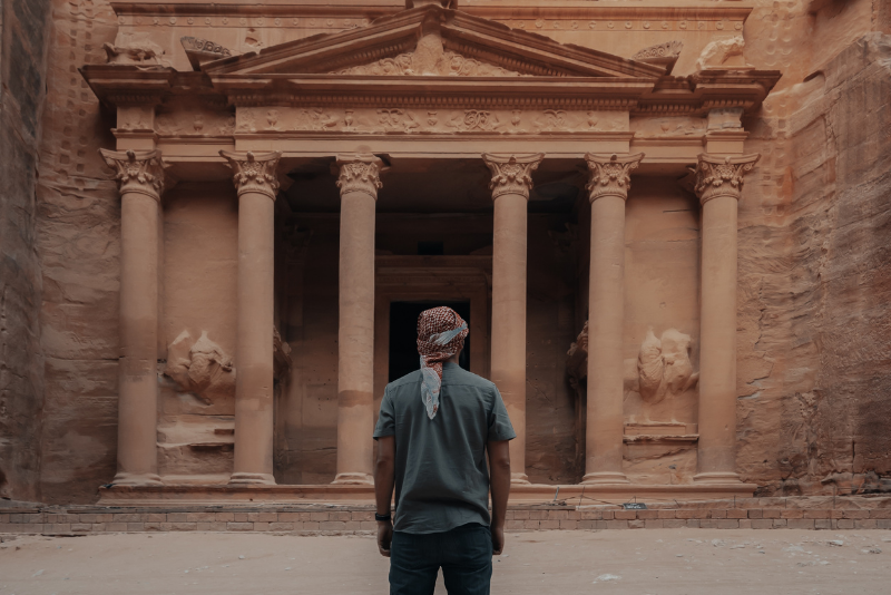 male in a headscarf standing in front of the historic Jordan Petra