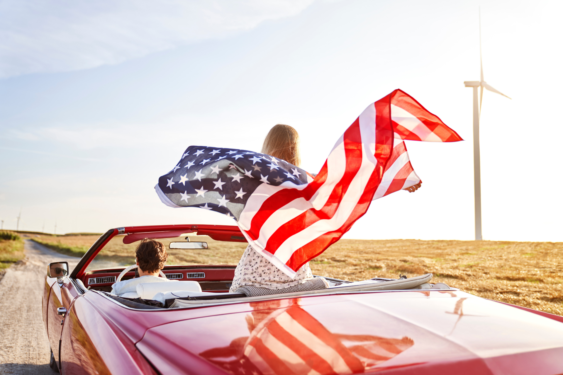 A lady flies a US flag from a convertible on a USA road trip