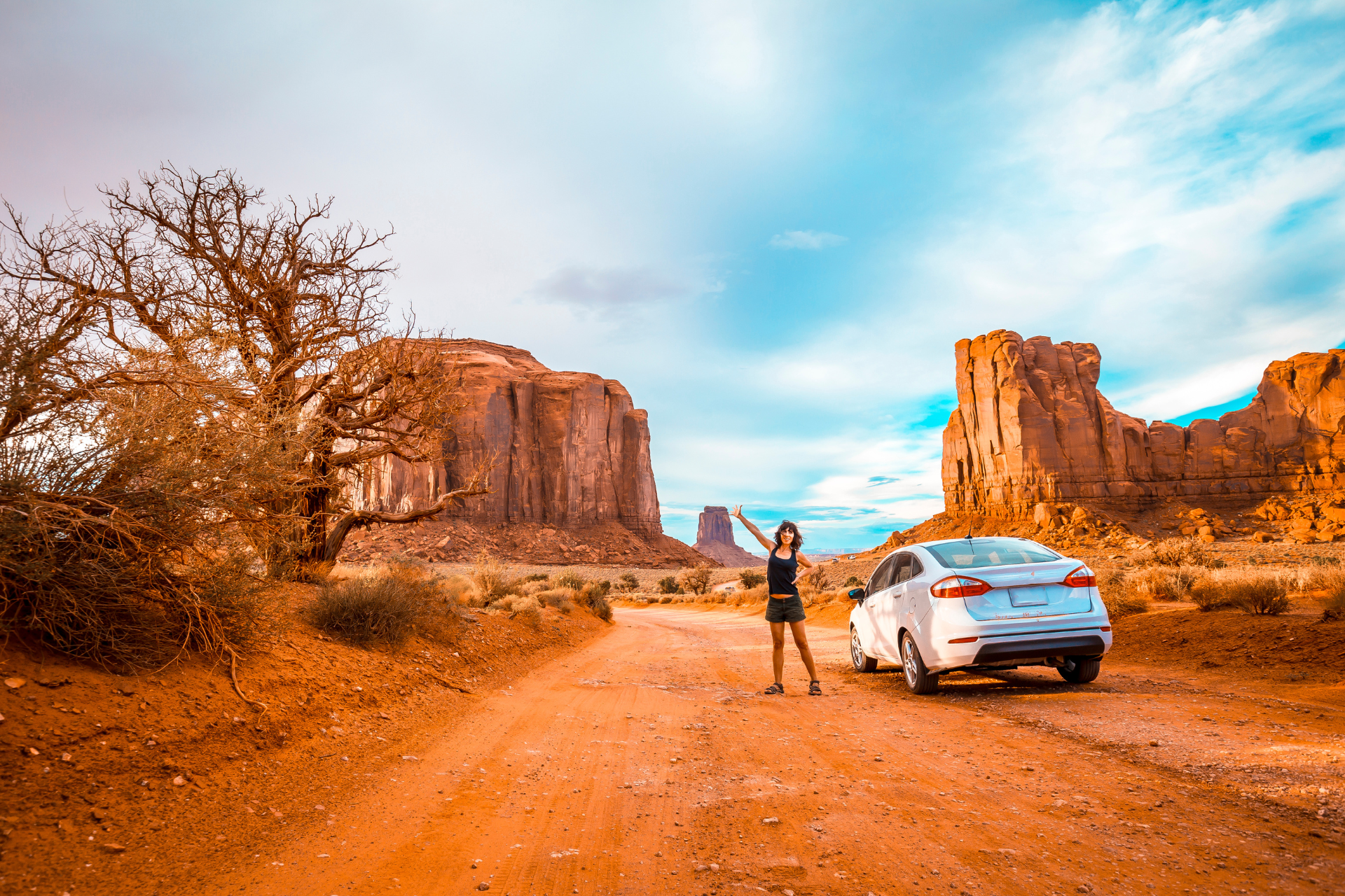 A tourist poses for a photo next to a car on a US west coast fly drive by Monument Valley